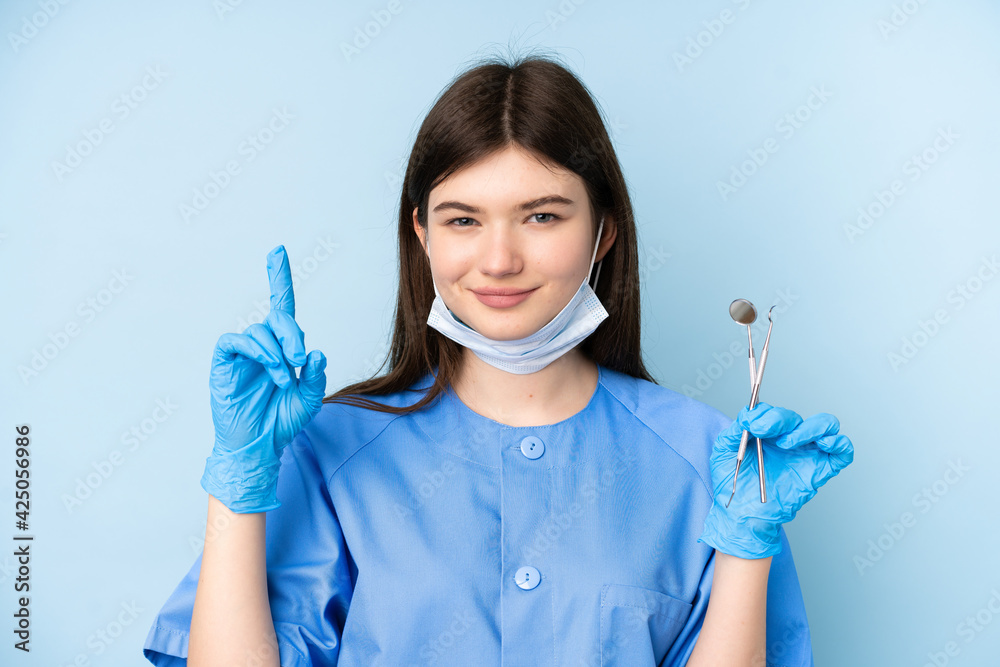 Young dentist woman holding tools over isolated blue background pointing with the index finger a great idea Young dentist woman holding tools over isolated blue background pointing with the index finger a great idea
