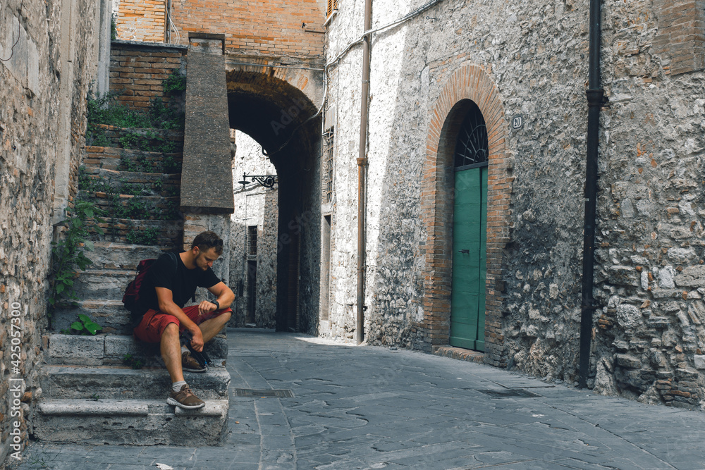A man sitting on the steps. Tourist. Narni (Terni, Umbria, Italy), medieval city: a typical old street