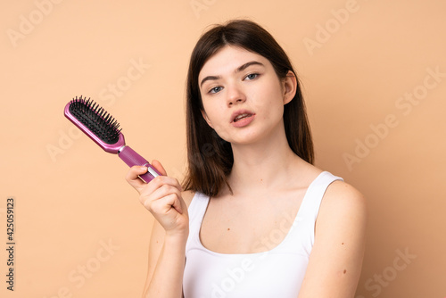 Young Ukrainian teenager girl over isolated background with hair comb