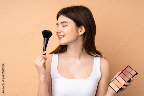 Young Ukrainian teenager girl over isolated background with makeup palette and happy
