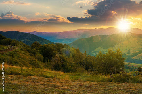 mountainous rural landscape at sunset. grassy meadow on top of a hill. clouds above the ridge in evening light. view in to the distant valley