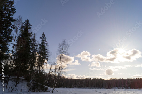 Beautiful winter (early spring)landscape with forest, frozen lake surface with pathway and the sun shining through the clouds.