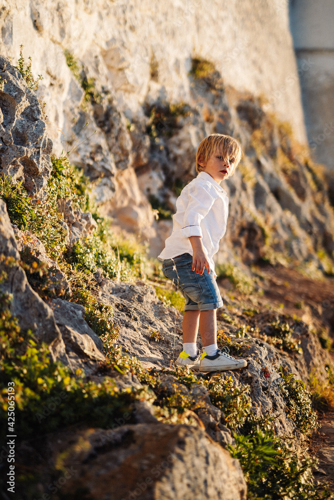 Jeune garçon, en chemise blanche, joue dans les rochers, en vacances, en été, grimpe, saute, escalade