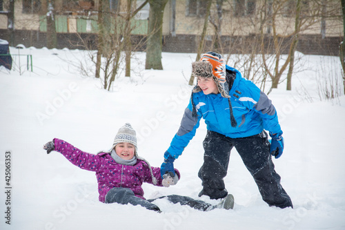 In winter  on the street  a brother helps his sister to climb out of a snowdrift.