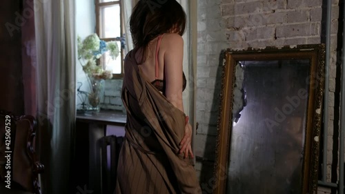 sexual half-naked lady is dancing alone in room with mirror, looking at herself, rear view of wriggling body