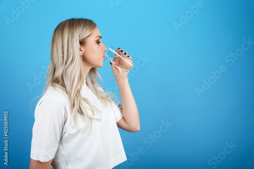 young woman drinks clear water from a glass on blue background close-up with copy space. girl in a white t-shirt drinks pure water on a colored background 