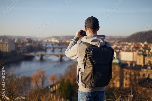 Man photographing urban skyline. Rear view of traveler against cityscape with Charles Bridge, Prague, Czech Republic.