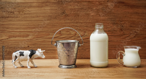 full metal bucket, glass milk bottle, cow and jugful on wooden background. photo