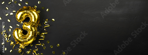 gold foil balloon number three or third. Birthday greeting card with the inscription 3. black concrete background. Celebrating the anniversary. Banner.