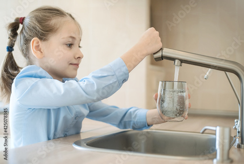 Little child is drinking fresh and pure tap water from glass. Water being poured into glass from kitchen tap. Zero waste and no plastic conscious minimalism lifestyle concept. Environment and ecology