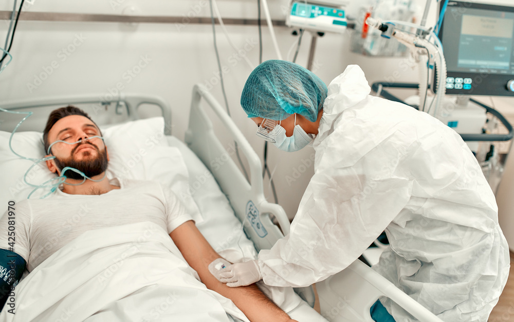 A doctor in a protective suit makes an injection into the vein of a patient suffering from coronavirus disease covid-19 in an intensive care unit. Treatment during a pandemic in a modern clinic.
