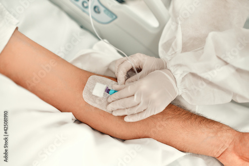 A doctor in a protective suit makes an injection into the vein of a patient suffering from coronavirus disease covid-19 in an intensive care unit. Treatment during a pandemic in a modern clinic.