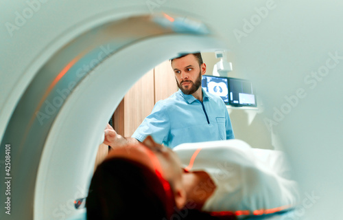 A patient lying on CT or MRI, the bed moves inside the machine, scanning her body and brain under the supervision of a doctor and a radiologist. In a medical laboratory with high-tech equipment.