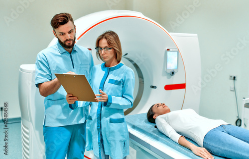 The patient lies on CT or MRI, the bed is moved inside the machine, scanning her body and brain under the supervision of a doctor and a radiologist. In a medical laboratory with high-tech equipment.