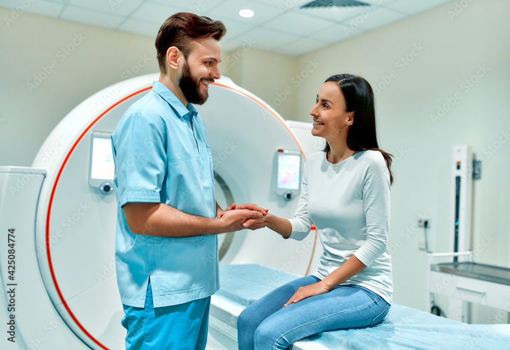 A caring radiologist talking to a patient who is sitting on a CT or MRI machine. In a medical laboratory with high-tech equipment. A caring radiologist talking to a patient who is sitting on a CT or MRI machine. In a medical laboratory with high-tech equipment.