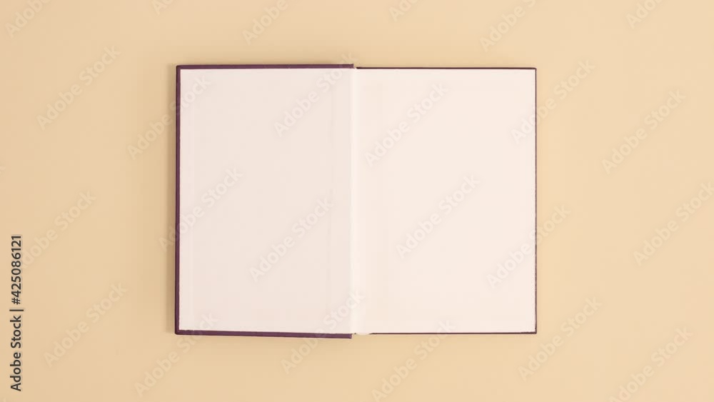 Purple hardcover vintage book appear and open with copy space on beige background. Stop motion flat lay
