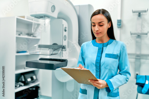 A female doctor with a patient card standing near the mammography apparatus. Health care and medical women concept.