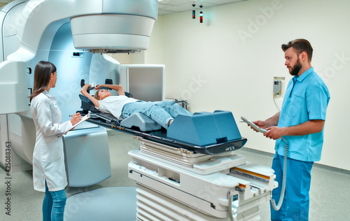 A young woman is undergoing radiation therapy for cancer under the supervision of doctors in a modern cancer hospital. Cancer therapy, advanced medical linear accelerator. photo