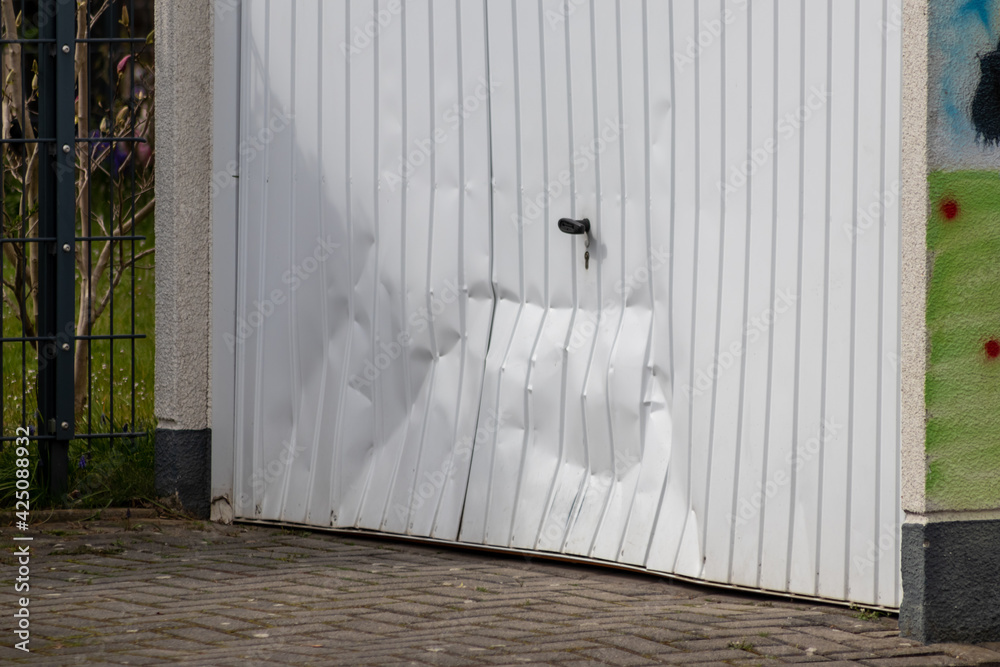 White damaged garage door shows the accident after a car crash when