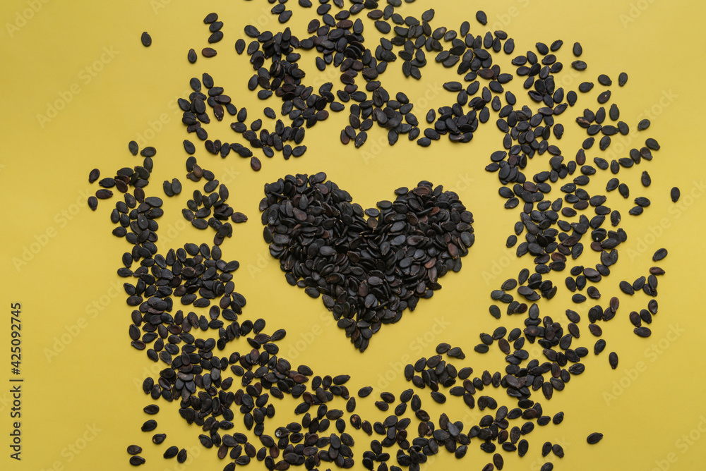 A pile of watermelon seeds on a yellow background in the shape of a heart A pile of watermelon seeds on a yellow background in the shape of a heart