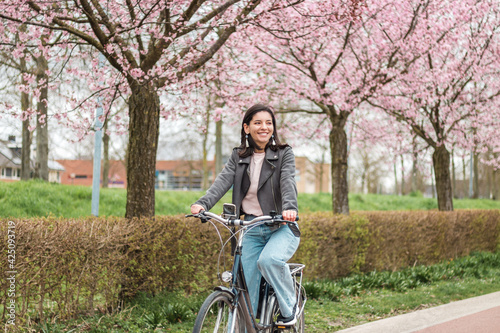 beautiful young woman of mixed races minority riding on bicycle in bloomy spring in casual clothes with attractive smile. lifestyle recreational portrait
