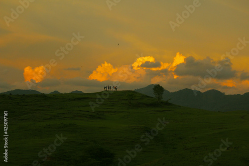 JENEPONTO INDONESIA, 23 March 2021: several people standing on the green hills looking at the clouds when the sun sets photo