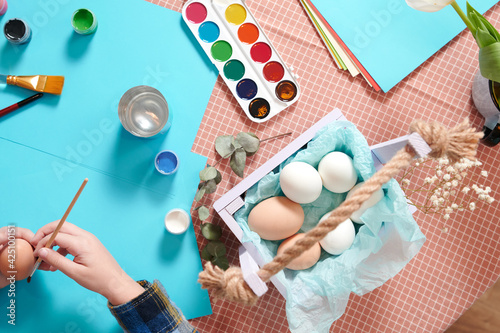 Easter table layout with eggs for painting.Top view of the hands of a child who paints festive easter eggs