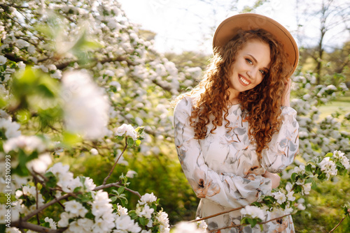 Happy smiling woman with the hat in blooming spring park. Spring fashion and lifestyle.