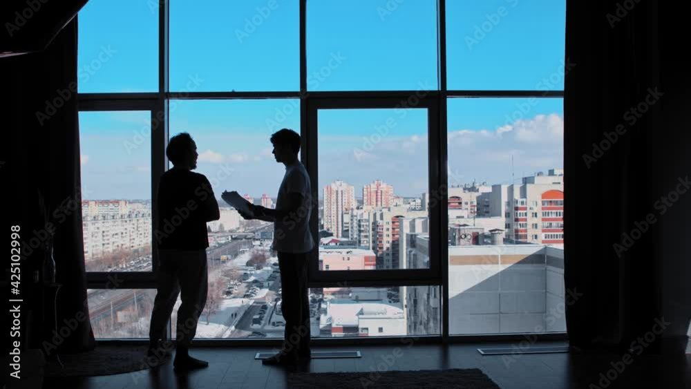 Two businessmen stand in an office with paronamy windows and discuss the deal Two businessmen stand in an office with paronamy windows and discuss the deal