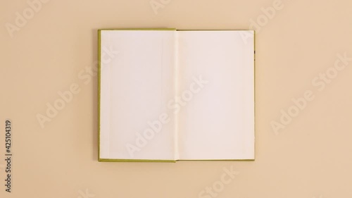 Bright green hardcover vintage book appear and open with copy space on beige background. Stop motion flat lay