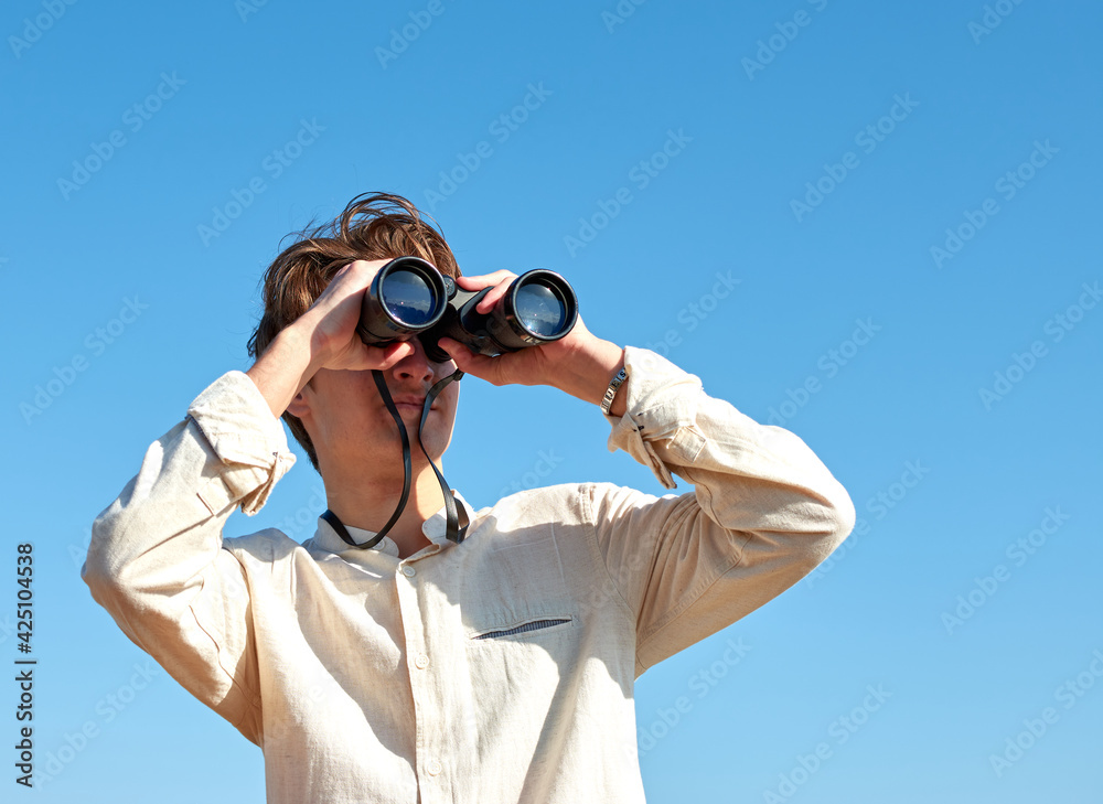 A young caucasian male looking at a view with binoculars under the bright blue sky A young caucasian male looking at a view with binoculars under the bright blue sky