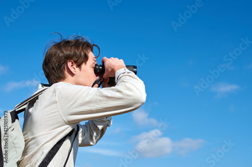 A close up of an attractive young explorer from Spain with a backpack in a white shirt observing through binoculars