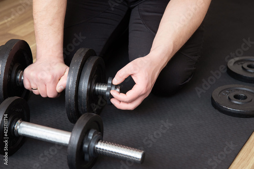 fitness, sport, weightlifting and bodybuilding concept - man assembling dumbbells at home
