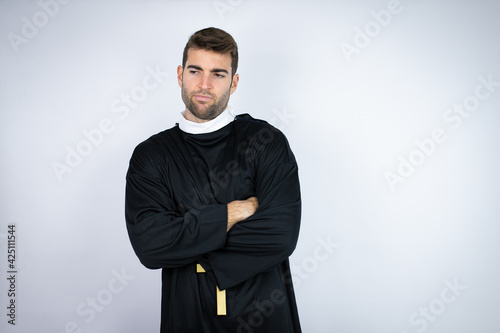 Young hispanic man wearing priest uniform standing over white background thinking looking tired and bored with crossed arms
