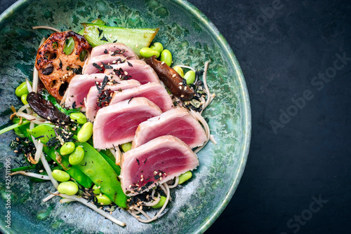 Modern style traditional Japanese gourmet seared tuna fish steak tataki with soba noodles and stir-fried vegetables served as top view on a Nordic design bowl with copy space right photo