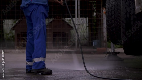Image of man cleaning under a truck with a power washer at a repair shop.