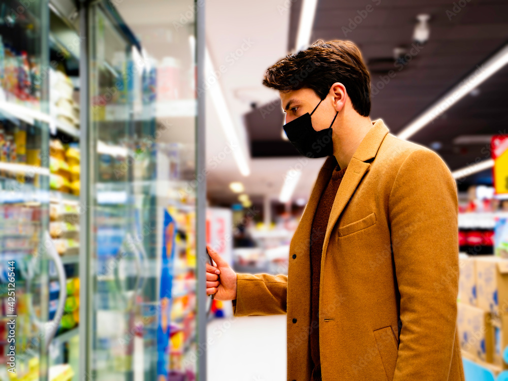 handsome man wearing a protective mask during the covid-19 in the supermarket taking groceries from the fridge handsome man wearing a protective mask during the covid-19 in the supermarket taking groceries from the fridge