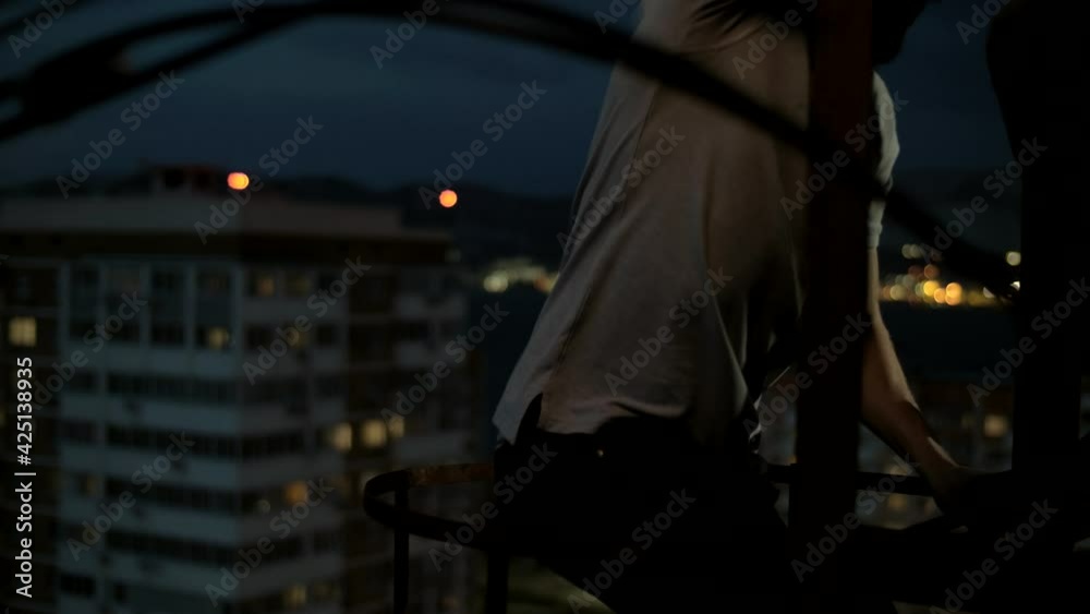 Man climbs on the roof of the facade stairs against the background of the lights of the night city Man climbs on the roof of the facade stairs against the background of the lights of the night city