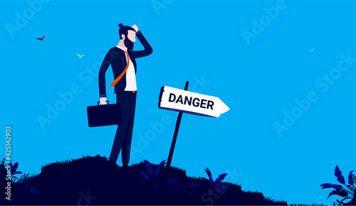 Business risk management - Businessman standing in front of sign pointing towards danger, thinking and contemplating. Dangerous path concept. Vector illustration.