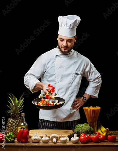 Handsome Italian chef tosses chopped vegetables in a frying pan