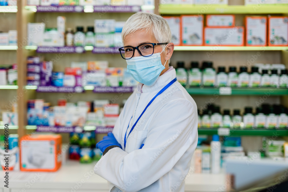 Senior female pharmacist with protective mask on her face working at pharmacy. Medical healthcare, Coronavirus, Covid-19 concept.
