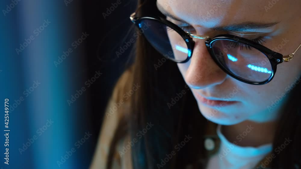 Portrait of focused young millennial female working at computer, reflection of laptop screen with eyeglasses, freelance girl browsing internet. Selective focus. Remote working from home concept