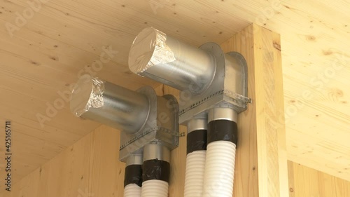 CLOSE UP: Close up shot of a recuperation system exchanger and two tubes running down a hardwood wall. Corrugated tubing runs out of the wooden wall of a modern low energy house under construction. photo