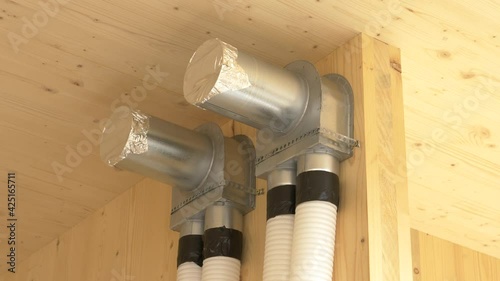 CLOSE UP: Close up shot of a recuperation system exchanger and two tubes running down a hardwood wall. Corrugated tubing runs out of the wooden wall of a modern low energy house under construction.