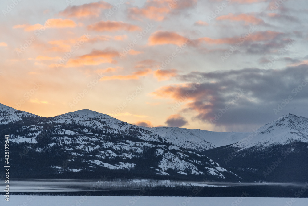 Stunning winter view in northern Canada during March, spring time with pink sunset views, wilderness mountains and frozen lake for tourism, tourist, travel background. 