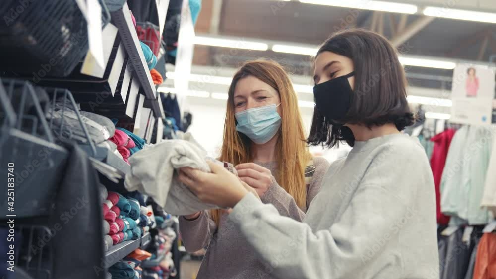 two girls in a mask in the store. coronavirus fashion clothing protected shopping concept. a two girls in mask at shop window makes purchases. safe pandemic coronavirus. girl in mask the store two girls in a mask in the store. coronavirus fashion clothing protected shopping concept. a two girls in mask at shop window makes purchases. safe pandemic coronavirus. girl in mask the store