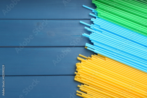 Colorful plastic drinking straws on blue wooden table, flat lay. Space for text