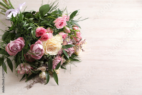 Beautiful bouquet with roses on light wooden table. Space for text