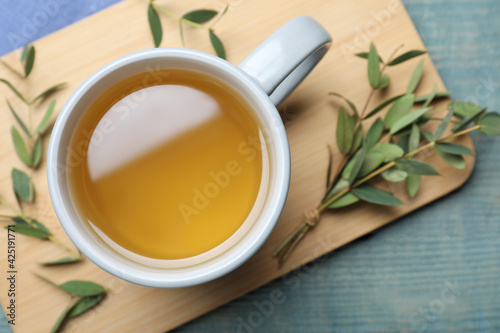Cup of aromatic eucalyptus tea on light blue wooden table, top view