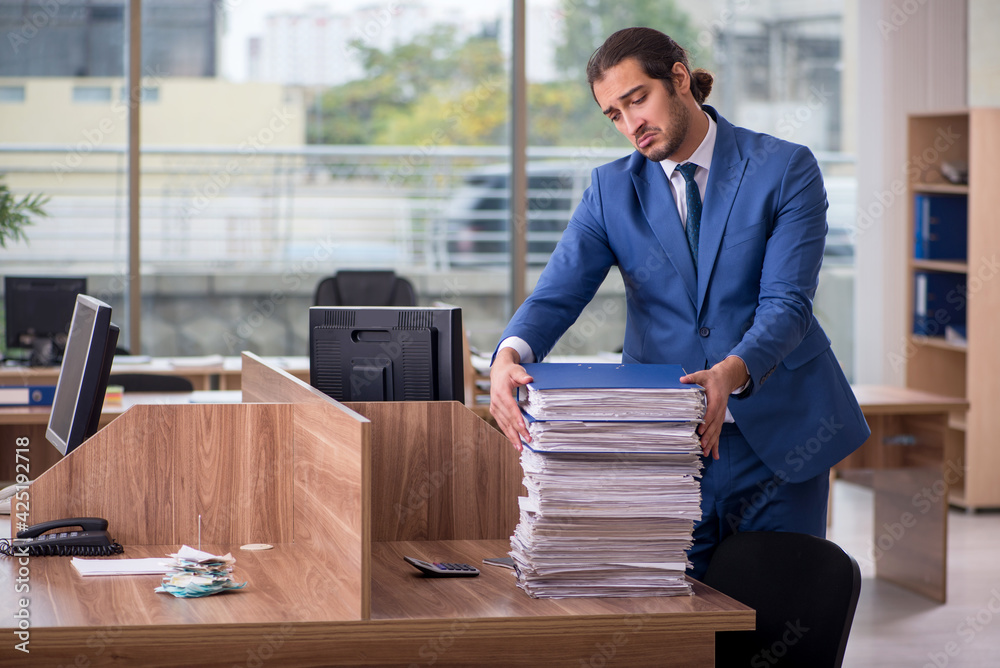 Young male employee unhappy with excessive work in the office Young male employee unhappy with excessive work in the office